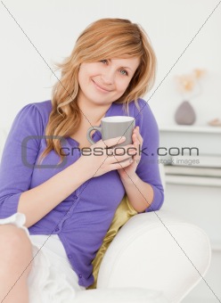 Good looking red-haired woman holding a cup of coffee while sitt