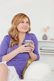 Beautiful red-haired woman holding a cup of coffee and posing wh