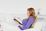 Pretty red-haired woman reading a book while lying on a sofa