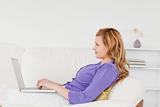 Beautiful red-haired woman using a laptop while lying on a sofa