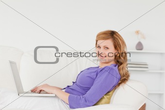Beautiful red-haired woman using a laptop and posing while lying