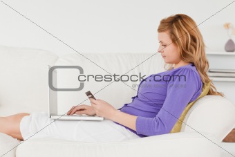 Beautiful red-haired woman using a laptop and phone while lying 