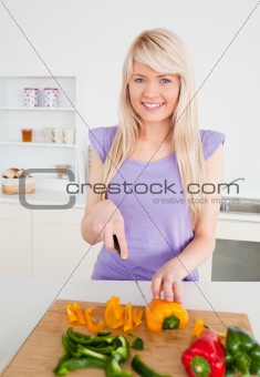 Beautiful blonde woman cutting peppers in modern kitchen interio