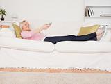 Attractive blonde woman watching tv while lying on a sofa