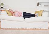Attractive blonde woman watching tv while lying on a sofa
