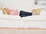 Attractive blonde female watching tv while lying on a sofa