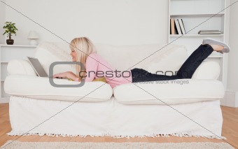 Young smiling woman relaxing with a laptop while lying on a sofa