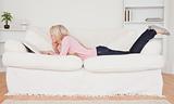 Young blonde woman relaxing with a book while lying on a sofa