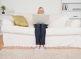 Young blonde woman relaxing with a laptop while sitting on a sof