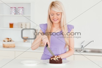 Smiling blonde female cutting a cake in a plate