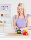 Attractive blonde female cutting vegetables in modern kitchen in