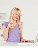 Beautiful woman drinking orange juice and relaxing on a laptop i