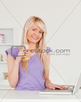 Beautiful female drinking orange juice and relaxing on a laptop 