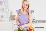 Smiling blonde woman cutting vegetables in modern kitchen interior