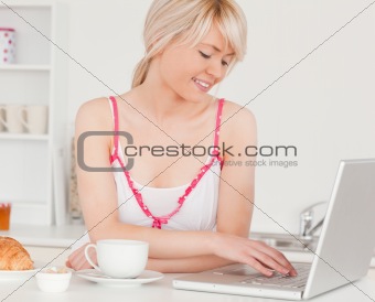 Beautiful female having her breakfast while relaxing with a lapt