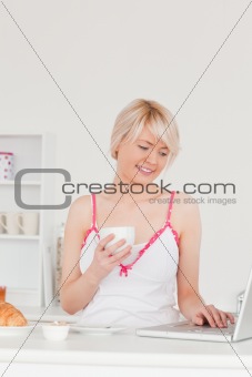 Attractive woman having her breakfast while relaxing with a lapt
