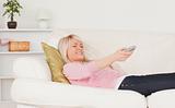 Good looking blonde female watching tv while lying on a sofa