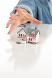 Womans Hand Reaching for Model House on a White Surface.