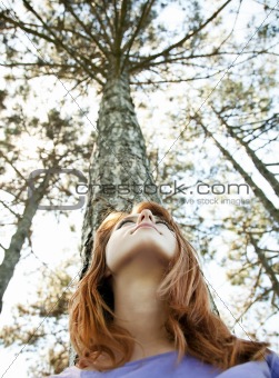 Beautiful redhead girl at the park in summer time looking up.