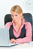 Concentrated business woman sitting at office desk and working on laptop
