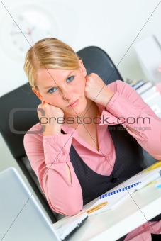 Bored business woman sitting at office desk and keep head on hands

