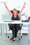 Excited  business woman sitting at office desk and rejoicing her success 
