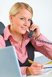 Smiling business woman sitting at office desk and talking on phone
