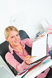 Smiling business woman sitting at office desk with document and pen for signing 
