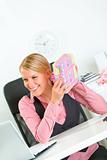 Pleased business woman sitting at office desk and holding gifts in hands
