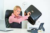 Shocked business woman sitting at office desk and searching something in briefcase 
