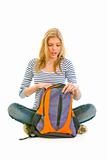 Teen girl sitting on floor and searching something in schoolbag
