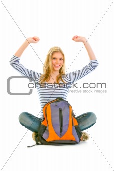 Pleased teengirl sitting on floor with schoolbag and rejoicing her success 
