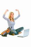 Sitting on floor with schoolbag and laptop pleased teengirl rejoicing her success 
