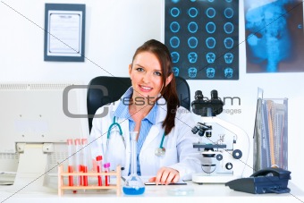 Smiling medical doctor woman sitting at table in her office
