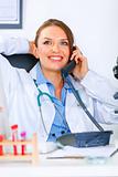 Relaxed doctor woman sitting at office table and talking on phone
