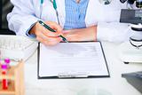 Medical doctor woman sitting at office table and working with document. Close up
