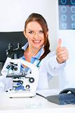 Smiling doctor woman using microscope in laboratory and showing thumbs up gesture
