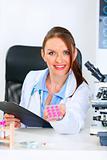 Smiling doctor woman sitting at office table and giving prescription drugs
