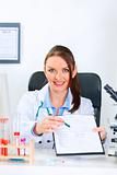 Smiling doctor woman sitting at office table with document and pen for signing   
