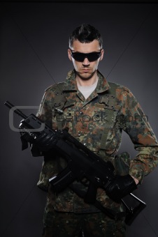 Young soldier in camouflage and ammunition with a rifle. studio 