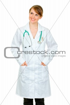 Smiling medical doctor woman with hands in pockets of robe looking at copy space
