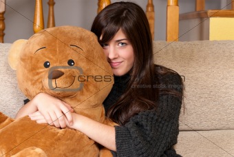 Young woman embracing teddy bear sitting on sofa close-up