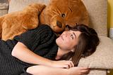 Young woman embracing teddy bear lying on on sofa close-up