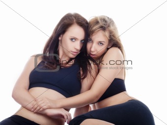 two young women sitting on the floor embracing each other - isolated on white