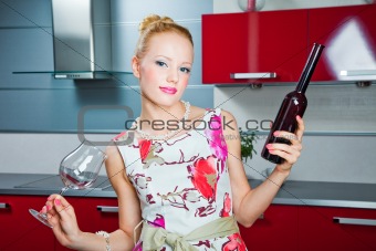 blonde girl with glass and bottle with wine in interior of red kitchen