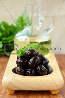 black olives and a bottle of oil on a wooden stand