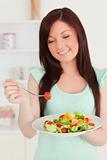 Beautiful red-haired woman enjoying a mixed salad in the kitchen