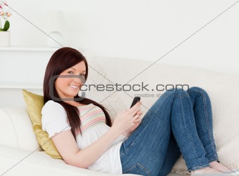 Pretty red-haired woman writing a text on her phone while lying 