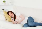 Good looking red-haired woman watching tv while lying on a sofa
