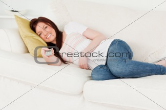 Beautiful red-haired woman watching tv while lying on a sofa